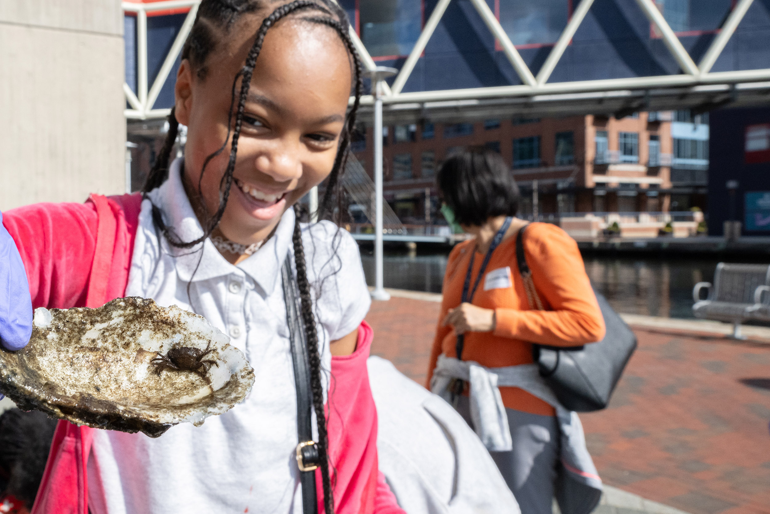 Young Girl Smiling While Holding an Oyster Shell With a Crab in it During the What Lives in the Harbor Program